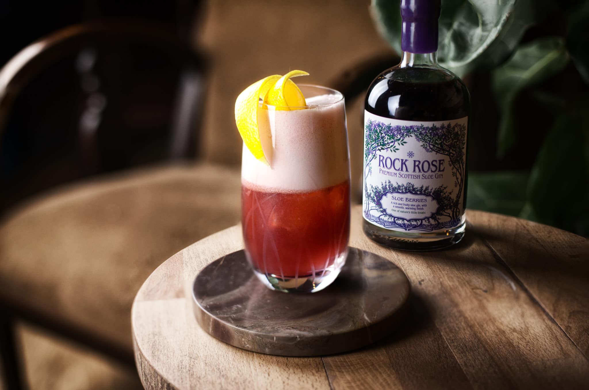 Bottle of Rock Rose Sloe Berries Gin and perfect serve in a large glass garnished with orange peel
