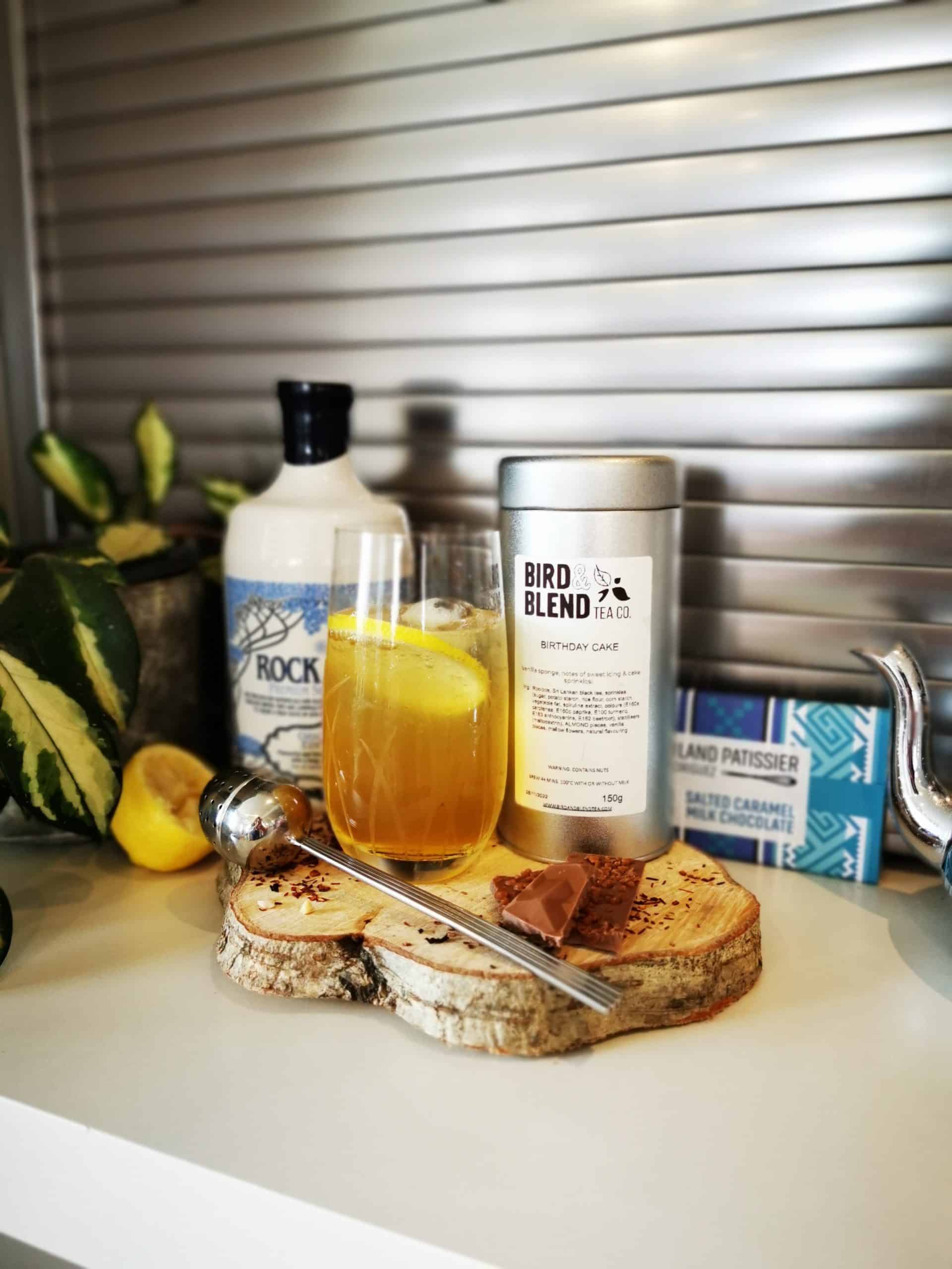 Bottle of Rock Rose Gin, box of Bird Blend "birthday cake" flavour and cocktail served in a tall glass